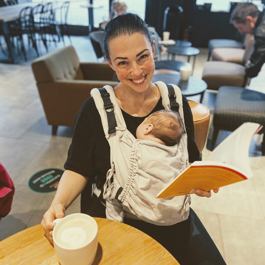 Fotka, jak sedím u stolu ve Starbucksu, na sobě mám nosítko s dvouměsíčním synem, který zrovna spinká. Jednou rukou si přidržuju hrnek s Café laté a v druhé držím knížku. Směju se do foťáku. 
