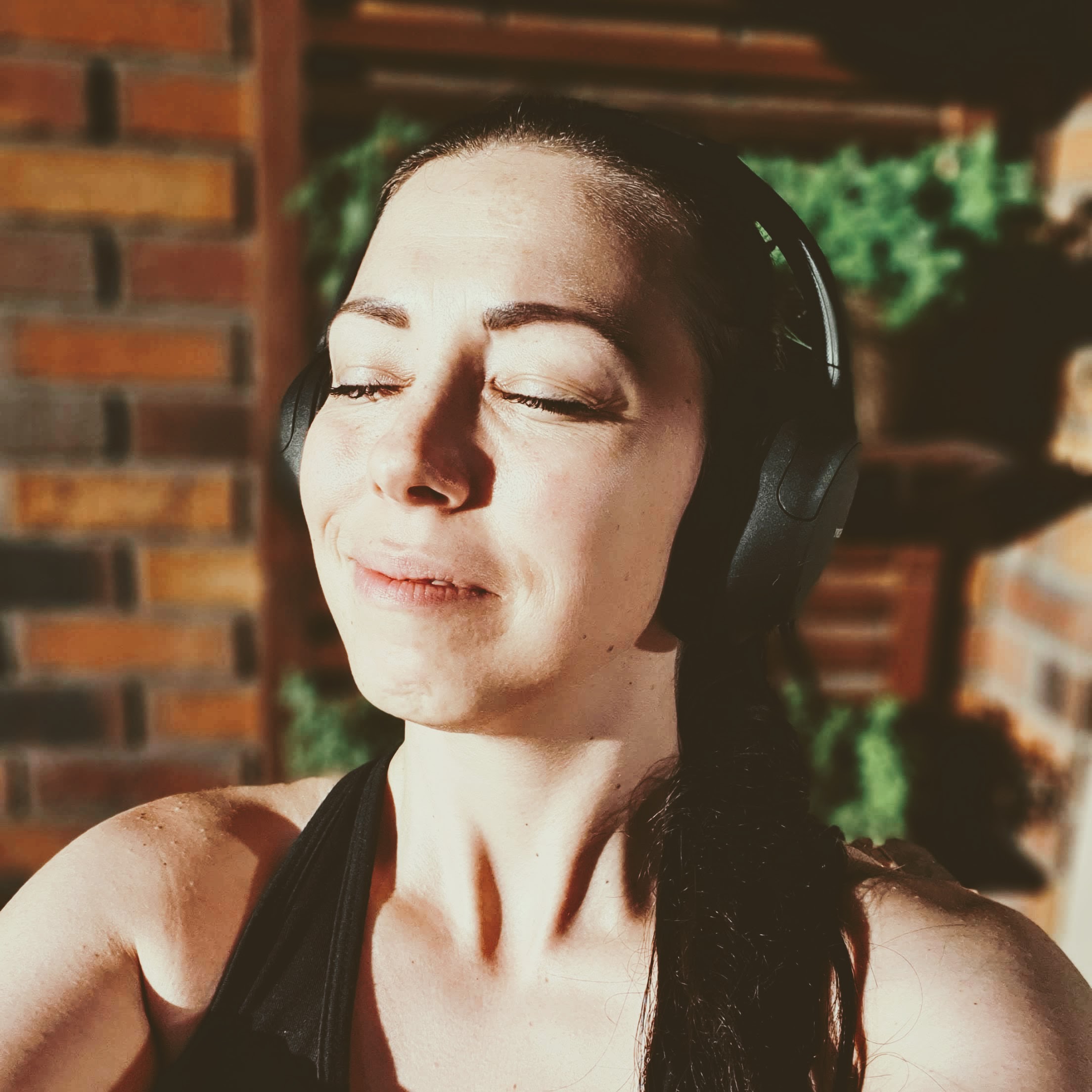 Fotka mě, jak se usmívám do sluníčka. Mám zavřené oči a na uších sluchátka s audioknihou.